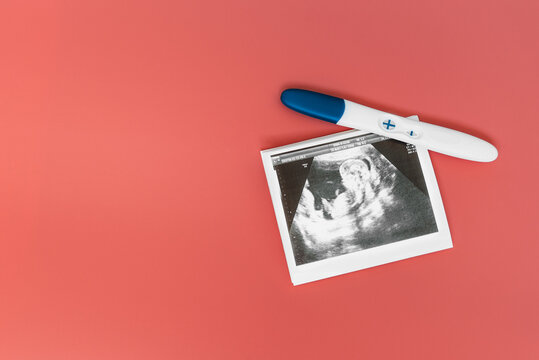 A positive pregnancy test and ultrasound photo on a pink background. A positive pregnancy test result. The pregnancy test shows a positive result. Ultrasound photos of the child. Copy space