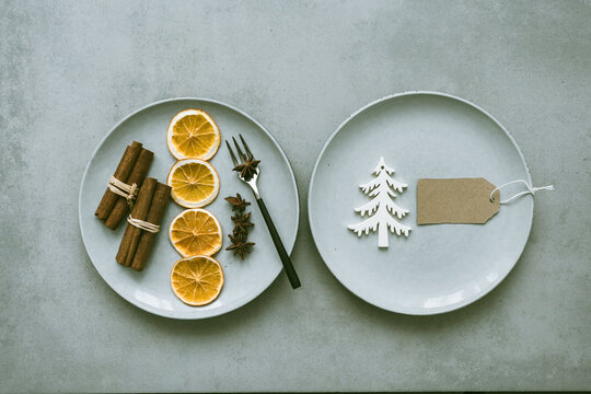 Zwei Teller mit getrockneten Orangenscheiben, Zimtstangen, Sternanis und iene unbeschriebene Tischkarte auf einem grauen Tisch. Modern, Draufsicht, Weihnachten.