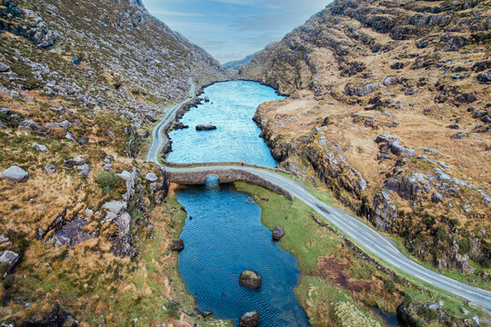 Aerial view of the stone Wishing Bridge over winding stream in green valley at Gap of Dunloe in Black Valley of Ring of Kerry, County Kerry, Ireland