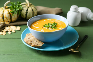 Bowl with delicious pumpkin cream soup, seeds and spices on color wooden background