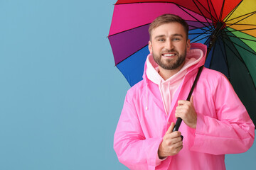 Young man in stylish raincoat and with umbrella on color background