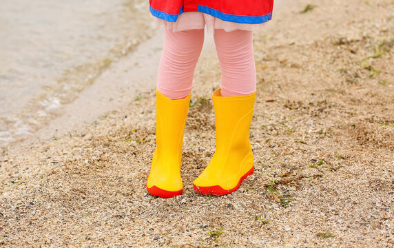Little girl in stylish rubber boots walking near river