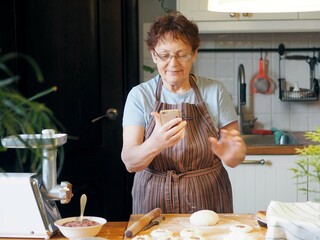 Portrait of an active elderly woman cooking in the kitchen and photographing her pastries. Healthy...