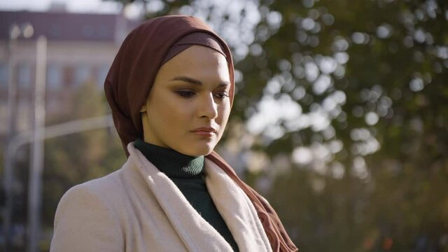 A young beautiful Muslim woman thinks about something in a park in an urban area - closeup