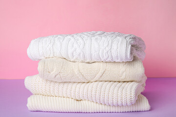 Stack of soft warm sweaters on table against color background