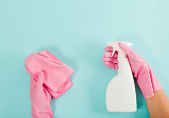 Cleaning bottle and washcloth in hands with pink rubber gloves. Blue background. Housekeeping and...