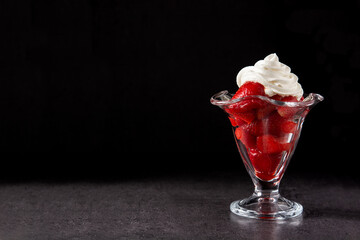 Strawberries and whipped cream in ice cream glass on black background