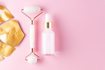 Massage quartz roller and pink glass bottle of cosmetic liquid transparent serum on pink background. Dropper bottle, hyaluronic acid, oil, serum. Facial massage and relaxation. Gua Sha massage tools.