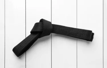 Fotobehang Tied black belt on white wooden background, top view. Oriental martial arts © New Africa