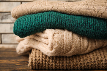 Fototapeta na wymiar Stack of different knitted sweaters on wooden table against brick wall background, closeup
