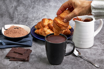 Hand of woman dipping a croissant in a cup of hot chocolate
