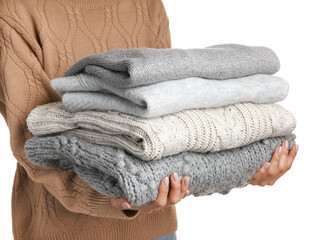 Young woman holding stack of stylish sweaters on white background, closeup