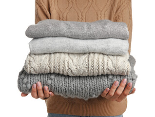 Young woman holding stack of stylish sweaters on white background, closeup