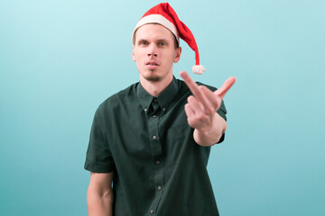 Young handsome man wearing a Santa hat over blue background showing middle finger doing fuck you...
