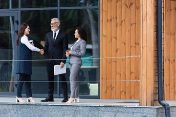middle aged businessman shaking hands with real estate agent near african american business partner