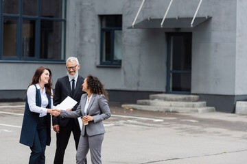 pleased african american businesswoman shaking hands with realtor near middle aged colleague outdoors