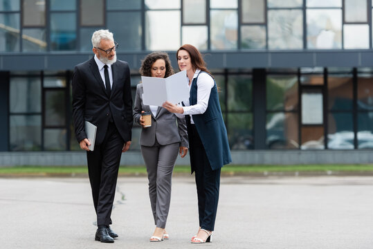 real estate agent showing documents to interracial business colleagues near blurred building