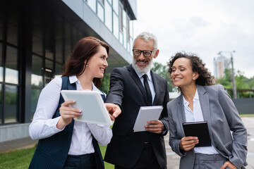 cheerful middle aged businessman pointing at digital tablet in hands of realtor near african...