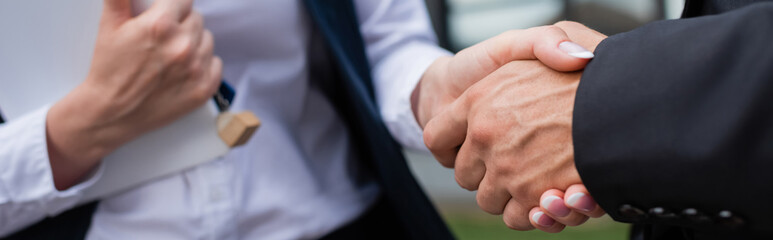 partial view of businessman shaking hands with blurred realtor with digital tablet and key...