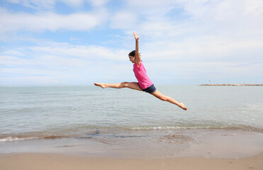 Caucasian girl performing difficult rhythmic gymnastics exercises and the split in the air on the beach