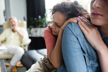 depressed african american woman leaning on lesbian girlfriend near blurred psychologist