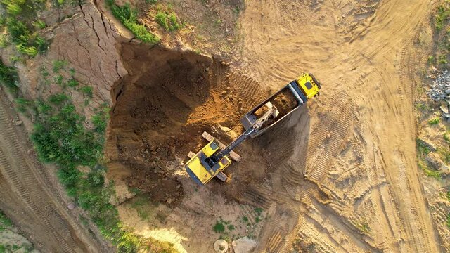 Excavator load the sand into dump truck, aerial view. Backhoe on earthworks. Open pit development and sand mining. Digging ground for foundation pit. Earthmoving at construction site.