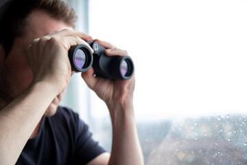 Man watching outside through his window with pair of binoculars.