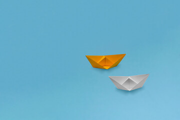 One yellow and one white paper ships (boats) of grainy paper on a blue background