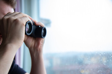 Man using binoculars and watching trough a window.