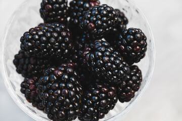 Fresh blackberries served in patterned clear glass bowl on gray background, concept of healthy eating vegan food. Closeup, top view, selective focus