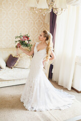 Pretty young Bride. Blonde-haired woman with wedding hair-style with a long tail. Boudoir morning of the bride. Looking to the camera or on her wedding bouquet