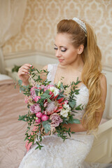 Pretty young Bride. Blonde-haired woman with wedding hair-style with a long tail. Boudoir morning of the bride. Looking to the camera or on her wedding bouquet