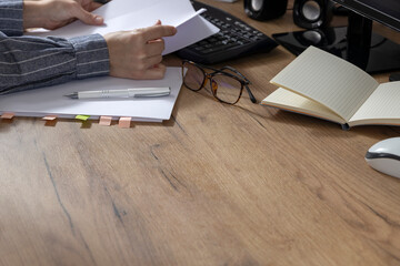 Woman holding and exploring business contract documents.Opened notebook,stack of papers,pen,glasses,keyboard on the wooden table.Empty space