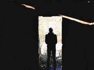 Silhouettes of man and doorway in the dark room with light going through it. Person’s silhouette entering the unknown. Abstract dark concrete interior with glowing door and human silhouette.