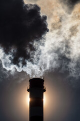 Dark smoke from chimney against the sun on sky