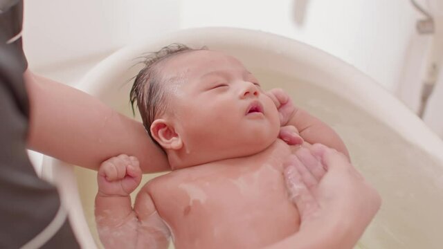 Calm of asian newborn baby bathing in bathtub.mother bathing her son in warm water.adorable newborn infant smile in tub relax and comfortable.Newborn baby care concept