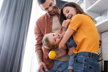 Happy child holding lemon near parents at home