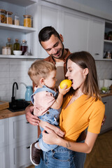 Toddler boy holding lemon near mother and dad at home