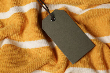 Blank grey tag on striped sweater, top view. Space for text