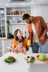 Man holding cherry tomatoes near family with smartphone and orange juice at home