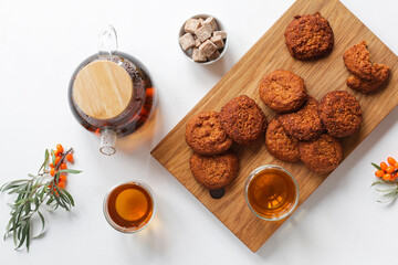 Vitamin tea with herbs and sea buckthorn, cereal gluten-free cookies with dried fruits on a wooden board. Healthy food, tea drinking.
White table, top view. 