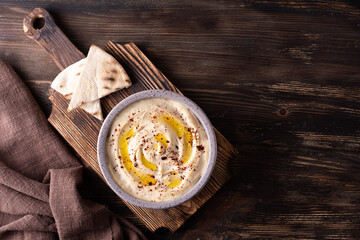 Hummus bowl and pita on cutting board on wooden table. - obrazy, fototapety, plakaty