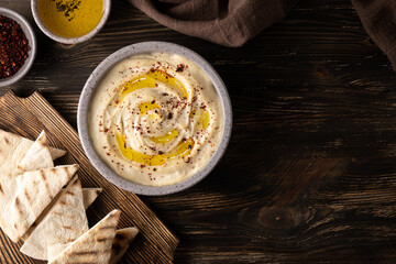 Chickpea hummus bowl, spices and pita on wooden background.