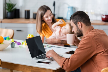 Man holding cup and using laptop near wife and son at home