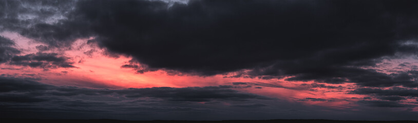 Panorama of dramatic colorful sunset with dark and bright clouds. The sun's rays are breaking...