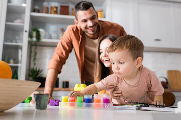Fototapeta premium Toddler kid taking paint near building blocks and parents at home