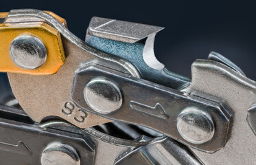 Sharp steel tooth of chainsaw chain detail on dark blue background. Closeup of metal chain link...