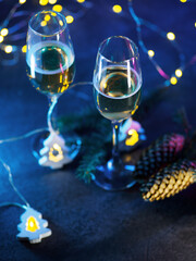 Two glasses of champagne, a Christmas composition. Blue background with a garland in the shape of a Christmas tree