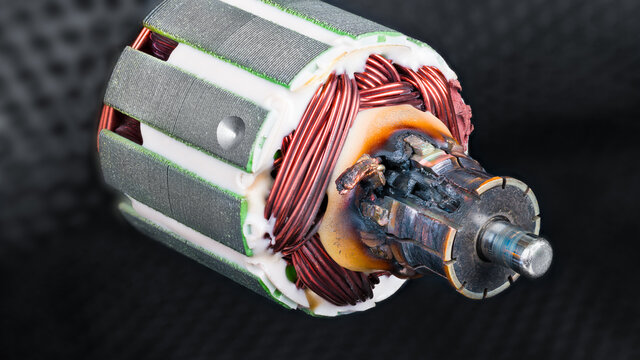 Damaged scorched commutator due to short circuit in rotor winding of DC electric motor. Detail of charred electromotor part with copper wire and metal laminations on blurred black netting background.