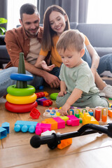 Kid playing with toys near blurred parents in living room